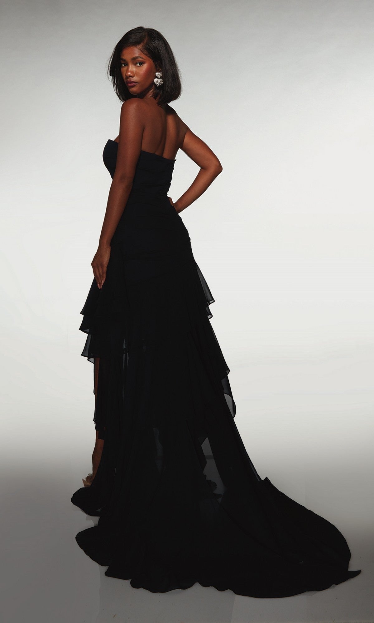 A woman poses with one hand on her hip against a light background, wearing the Alyce 62153 long formal dress, featuring a strapless design and layered train.